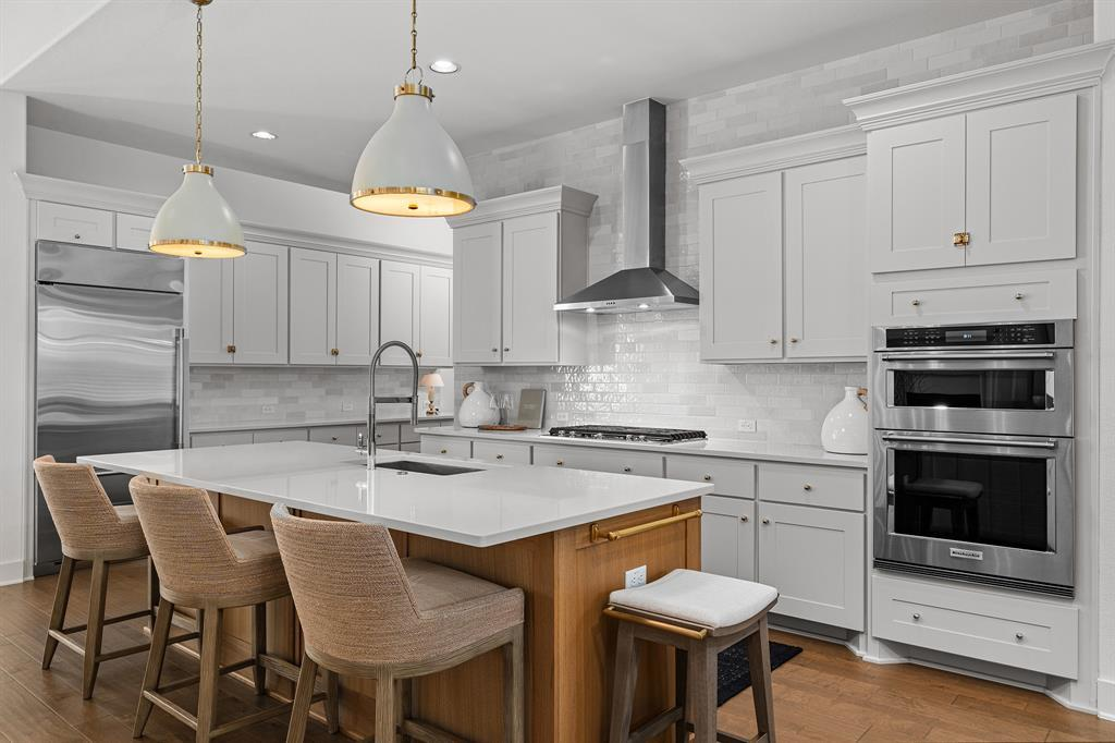 Kitchen island with seating, range hood, double wall ovens and subway tile backsplash